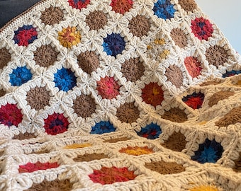 May include: A crocheted throw blanket with a granny square pattern in beige, brown, red, yellow, and blue.