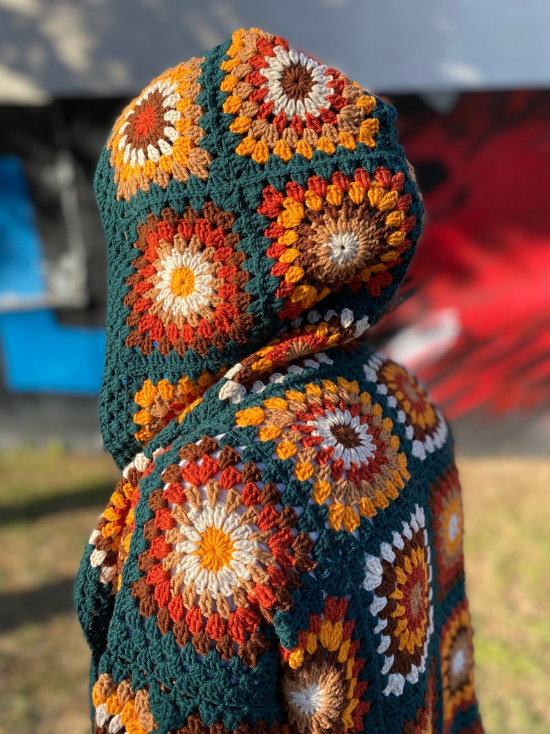 May include: A green crocheted hooded cardigan with a colorful geometric pattern. The cardigan is made with a variety of shades of brown, orange, yellow, and white.