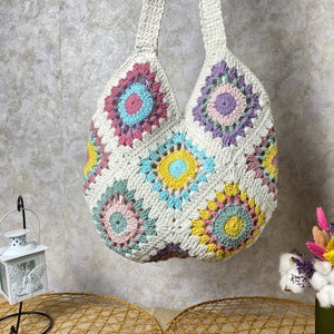 May include: A white crocheted tote bag with colorful floral designs. The bag has a wide, open top and two long straps.