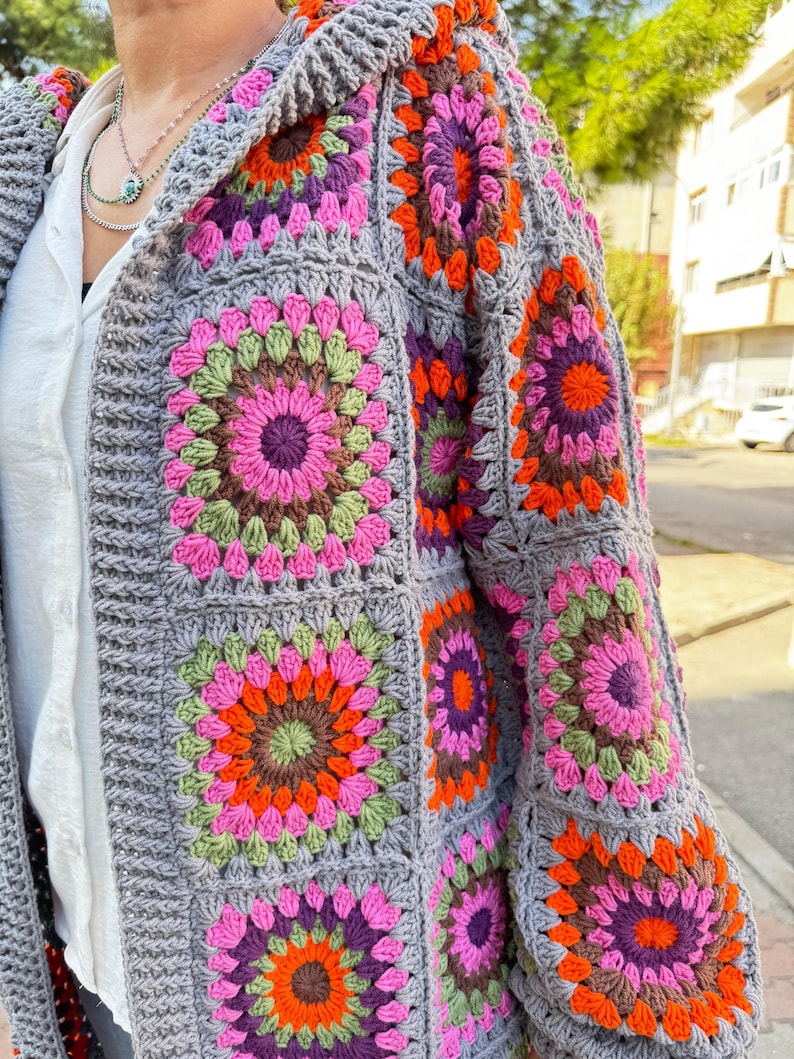 May include: A gray crochet cardigan with a hood, featuring colorful granny square patterns in shades of pink, orange, green, and purple.