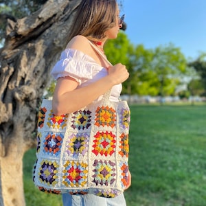 May include: A white crochet tote bag with colorful granny squares. The bag has a variety of colors including red, orange, yellow, green, blue, and purple.