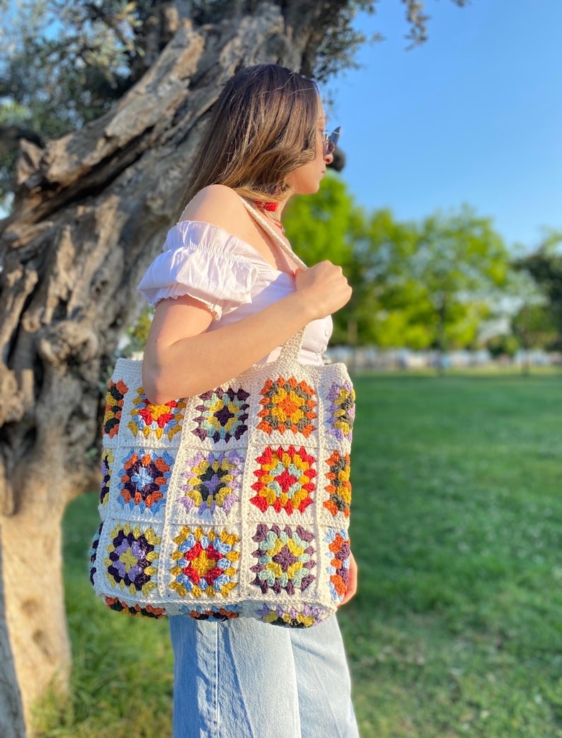 May include: A white crochet tote bag with colorful granny squares. The bag has a variety of colors including red, orange, yellow, green, blue, and purple.