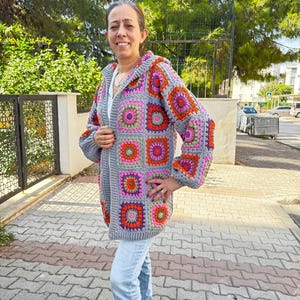 May include: A gray crocheted cardigan with a hood, featuring a colorful geometric pattern of squares in shades of pink, orange, green, and purple.