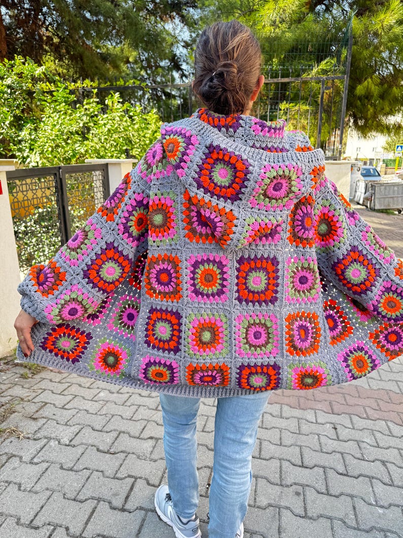 May include: A gray crochet cardigan with a hood, featuring a colorful geometric pattern of squares with pink, orange, green, and purple accents.