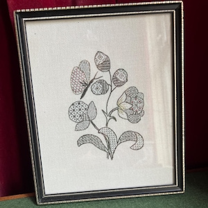 May include: Framed floral embroidery featuring a butterfly and flowers in shades of black, pink, and green. The artwork is set against a white background and framed in a black and silver rectangular frame. The embroidery is detailed and intricate.