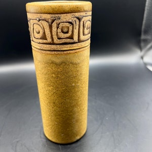 May include: A brown ceramic vase with a geometric pattern around the top.