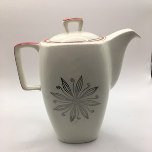 May include: White ceramic teapot with a red and black trim. The teapot features a stylised flower design in silver on the front.
