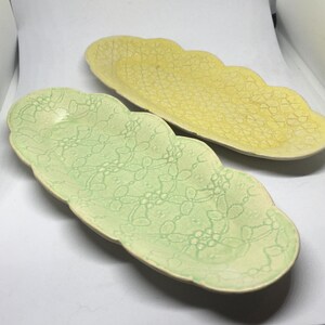 May include: Two ceramic serving dishes with scalloped edges. The larger dish is yellow with a floral pattern. The smaller dish is green with a floral pattern.