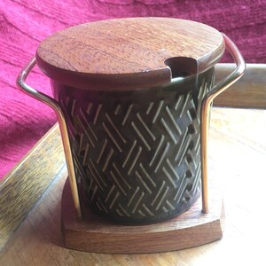 May include: A dark green ceramic jar with a woven pattern, a wooden lid with a small spout, and a gold metal stand with a wooden base.
