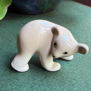 May include: A small, white ceramic figurine of a bear cub. The bear is standing on all fours and has black eyes. The figurine is glazed and has a smooth finish.