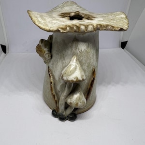 May include: A ceramic vase shaped like a mushroom with a wide, flat top and three smaller mushrooms on the side. The vase is glazed in a white and brown colour.