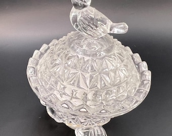 May include: A clear glass candy dish with a bird finial on the lid. The dish has a scalloped edge and sits on three feet.