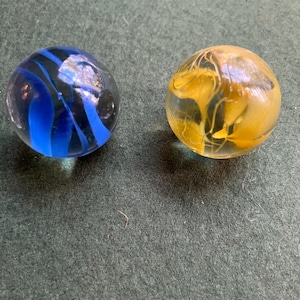 May include: Two spherical glass marbles. One marble is clear with deep blue swirling patterns inside. The second marble is clear with golden-yellow swirling patterns inside. Both objects are smooth, round, and feature internal color designs.