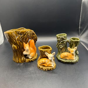 May include: A collection of ceramic figurines featuring woodland creatures. Includes a squirrel, a fawn, and a deer, all resting on or near tree stump-shaped vases. The color palette is primarily brown, orange, and green.