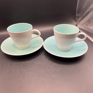 May include: Two light blue teacups with white interiors and matching saucers. The cups and saucers have a subtle ombre effect.