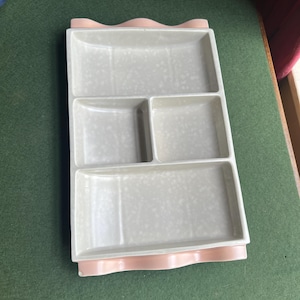 May include: A light gray ceramic serving tray with four compartments. The tray has a pink scalloped edge.