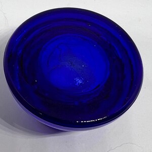 Puede incluir: Un cuenco de vidrio circular azul oscuro. El cuenco tiene una forma redondeada con una superficie lisa y brillante. El color es un azul rico y saturado, con sutiles variaciones de tono. El cuenco parece estar vac&iacute;o y est&aacute; sobre una superficie blanca.