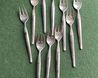 May include: A set of nine silver-toned dessert forks with a textured handle. The forks are arranged on a green surface.