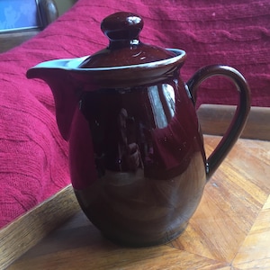 May include: A brown ceramic teapot with a lid and a handle. The teapot has a glossy finish.