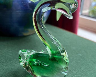 May include: A green glass swan figurine with a clear glass body and a green glass head and neck.