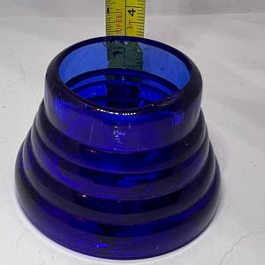 Puede incluir: Un objeto de vidrio azul cobalto con un dise&ntilde;o c&oacute;nico acanalado. El objeto mide aproximadamente 5 cm de alto y tiene una abertura ancha. El vidrio tiene un acabado brillante. Se coloca una cinta m&eacute;trica junto al objeto.