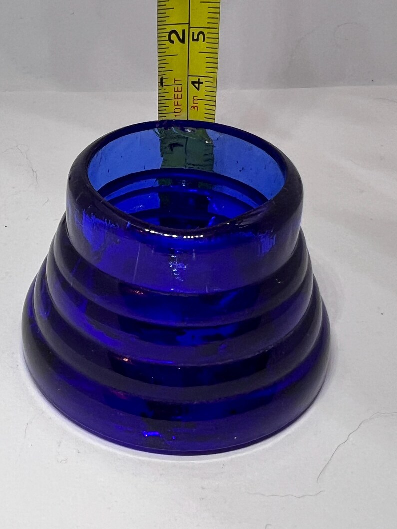 Puede incluir: Un objeto de vidrio azul cobalto con un dise&ntilde;o c&oacute;nico acanalado. El objeto mide aproximadamente 5 cm de alto y tiene una abertura ancha. El vidrio tiene un acabado brillante. Se coloca una cinta m&eacute;trica junto al objeto.