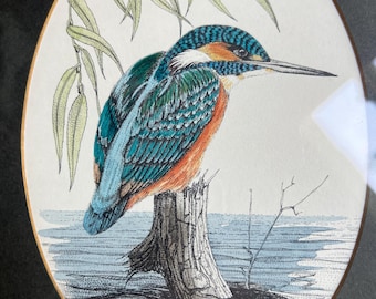May include: An oval framed print of a kingfisher bird perched on a tree stump, with a willow branch overhead. The bird has blue, teal, and orange plumage. The artwork is signed and dated 1972, with the word "KINGFISHER" below.