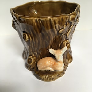 May include: A brown ceramic planter shaped like a tree stump with a small deer figurine on the front. The planter has a rough, textured surface and is ideal for displaying small plants.