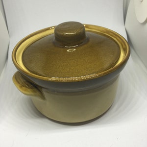May include: A brown ceramic casserole dish with a lid. The dish has a light brown glaze and a darker brown rim. The lid has a knob on top.