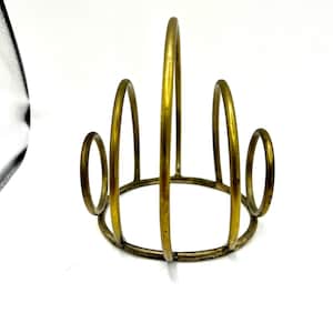 May include: A gold metal ring holder with a circular base and four curved loops. The holder is designed to hold multiple rings.