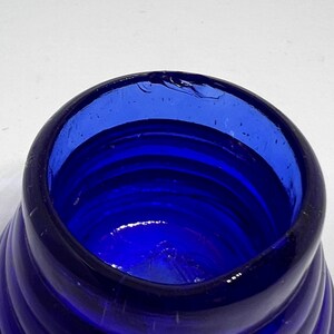 Puede incluir: Primer plano de una botella de vidrio azul cobalto con un dise&ntilde;o en espiral. El borde de la botella tiene una peque&ntilde;a astilla. El vidrio es de un color azul profundo y rico, y el patr&oacute;n en espiral crea un efecto texturizado. Para uso decorativo o funcional.