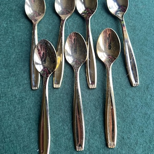May include: Set of seven gold-tone teaspoons. The spoons are arranged in a fan shape on a green surface.