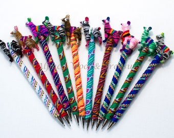 May include: A set of 12 colorful pens with animal toppers. The pens are wrapped in colorful woven fabric and feature animal toppers such as zebras, llamas, and giraffes.