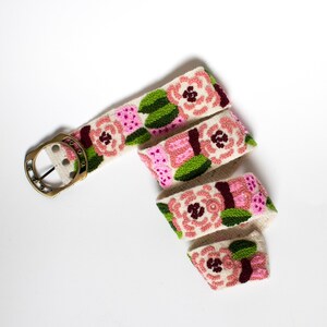 May include: A white fabric belt with a gold buckle and embroidered pink and green flowers.
