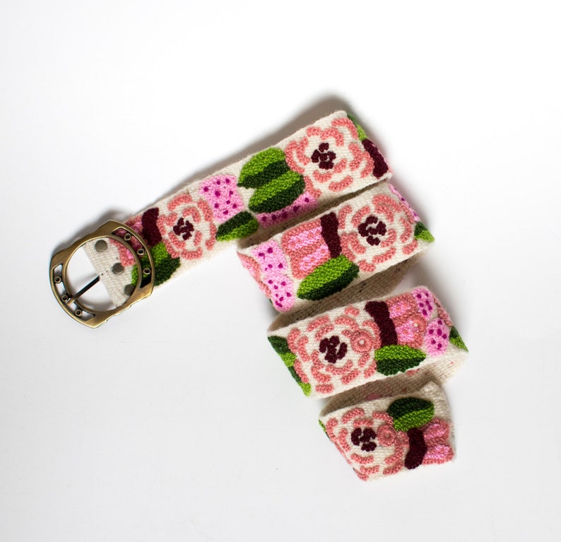 May include: A white fabric belt with a gold buckle and embroidered pink and green flowers.