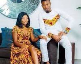 May include: A couple wearing matching white and yellow patterned outfits. The man is wearing a long-sleeved shirt with a white collar and white trousers. The woman is wearing a long dress with a yellow and red pattern.
