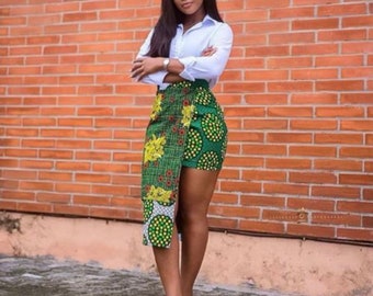 May include: A woman wearing a white button-down shirt and a green and yellow patterned skirt with a high slit. The skirt has a geometric design with circles and flowers.