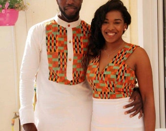 May include: A couple wearing matching white outfits with colourful patterned accents. The man is wearing a long-sleeved shirt with a button-up collar and the woman is wearing a sleeveless dress with a V-neckline. Both outfits feature a geometric pattern in shades of orange, green, black, and white.