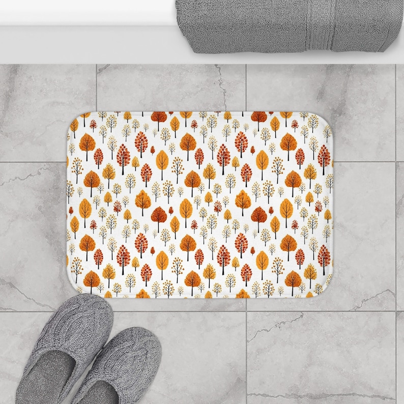 May include: White bath mat with a repeating pattern of orange and yellow trees. The trees are stylized and have a simple design.