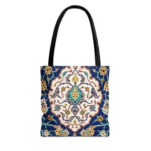 Puede incluir: Un bolso tote con asa negra y un patrón ornamental. El diseño presenta un medallón central con elementos florales y geométricos en tonos azules, blancos, amarillos y turquesas. El fondo del bolso es azul oscuro.