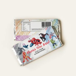 Könnte beinhalten: Ein bunter Schokoladenriegel-Wrapper mit einem Aquarellhintergrund, auf dem Superheldenfiguren zu sehen sind. Der Wrapper lautet "Oliver's Hero Bars! Fuel your superpowers!"