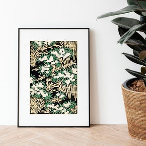 May include: A black framed print with a white background and a floral pattern in shades of green and white. The print is hanging on a white wall next to a potted rubber plant with dark green leaves.
