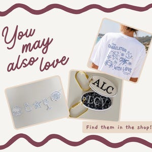 May include: A white t-shirt with blue coastal graphics and the text 'from CHARLESTON WITH LOVE', a garland of white shell and starfish shapes, and two oval keychains with gold rings featuring the monogrammed letters 'ALC' and 'LCV'.