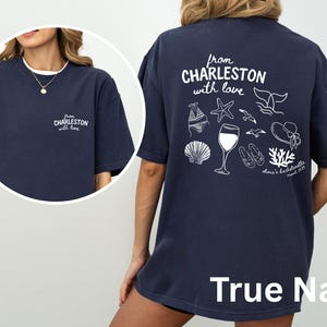 May include: A navy blue t-shirt featuring white screen-printed graphics. The front displays the text 'from CHARLESTON with love'. The back shows the same text above illustrations of a bikini, starfish, whale tail, wine glass, seagulls, sun hat, seashell, sandals, and coral, with 'Olivia's bachelorette august 2025'.