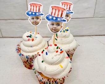 Puede incluir: Tres cupcakes con glaseado blanco y chispas de colores coronados con sombreros de Tío Sam rojo, blanco y azul con la cara de un niño en cada uno.