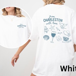 May include: A white t-shirt featuring blue graphics. The back displays the text "from CHARLESTON with love" above illustrations of a bikini, starfish, whale tail, wine glass, seashell, sandals, coral, and sun hat, with "olma's bachelorette" below.
