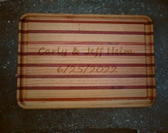 May include: A wooden cutting board with a natural wood finish and red stripes. The board is engraved with the text "Carly & Jeff Heim 6/25/2022".