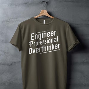 以下が含まれることがあります： 前面に白い文字で「Engineer Professional Overthinker」とプリントされた濃い緑色のTシャツです。