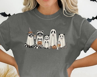 Peut inclure: T-shirt gris foncé avec un motif sur le thème d'Halloween. Le motif représente des ratons laveurs et un panda déguisés en fantômes, tenant des citrouilles et des bougies. Le t-shirt a une coupe décontractée et des manches courtes.