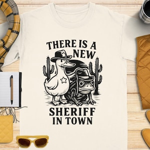 新しい保安官Tシャツ、おどけたガチョウとカエルのカウボーイ、ウエスタンシャツ、面白い保安官シャツ、漫画動物シャツ、AIデザインTシャツ
